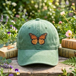 Può includere: Un berretto da baseball verde salvia con una farfalla monarca ricamata sul pannello frontale. Il berretto presenta una corona strutturata, una visiera curva con cuciture a vista e un classico design a sei pannelli con occhielli.