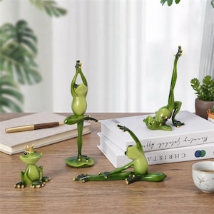 Puede incluir: Cuatro figuras de ranas verdes en varias posturas. Una rana pequeña lleva una corona dorada. Una está de pie sobre un nenúfar con los brazos levantados. Una está tumbada de lado con una pierna hacia arriba. Una está sentada con los brazos estirados.