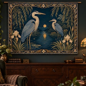May include: A rectangular wall tapestry featuring two blue herons standing in a dark blue river at night under a full moon. The scene is framed by willow branches and white iris flowers, with a decorative gold-toned border on all four sides.