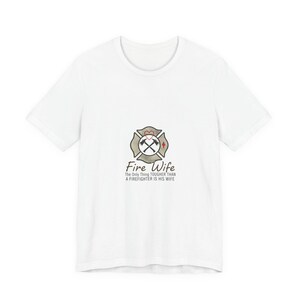 May include: White t-shirt with a firefighter emblem, a heart, and crossed axes. The text "Fire Wife" is below the emblem, with the phrase "The Only Thing TOUGHER THAN A FIREFIGHTER IS HIS WIFE."
