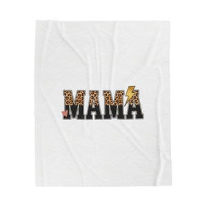 Op de afbeelding: Witte deken met het woord "MAMA" in een vet, decoratief lettertype. De letters "M" en "A" hebben een luipaardprintpatroon, terwijl de andere letters zwart zijn. Een gouden bliksemschicht en een klein roze hart accentueren het ontwerp.