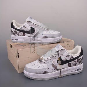 Peut inclure: Baskets Air Force 1 blanches et grises avec des détails noirs et un design unique. Les baskets présentent un logo Nike noir, des graphismes de style bambou et le mot "AIR" sur le côté. Elles sont présentées sur une boîte avec le texte "CULT. CUSTOM".