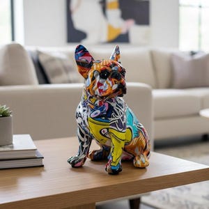 Peut inclure: Figurine de bouledogue français de style pop art coloré. La sculpture présente un mélange de couleurs vives, dont le jaune, le bleu, l'orange et le blanc. Le chien est assis sur une table basse en bois dans un salon.