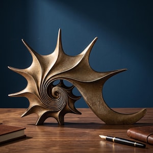 Peut inclure: Sculpture abstraite de couleur bronze, avec un motif en spirale d'un côté et une forme incurvée en forme d'aile de l'autre. Posée sur une surface en bois, avec un fond bleu foncé.