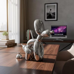 May include: A polished silver balloon dog sculpture and a small matching object sit on a wooden desk. The sculpture is a whimsical representation of a dog, with a smooth, reflective surface. The desk is in a well-lit room with a window and a computer.