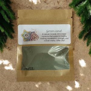 May include: A brown paper packet with a clear window, filled with green powder. A white label reads "Greensand" and provides product details. The label also features a cartoon hermit crab and the words "K's Happy Hermits".