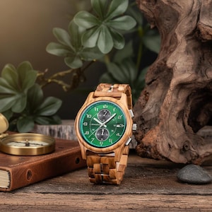 Peut inclure: Une montre-bracelet en bois avec un cadran vert et un bracelet en bois. La montre a des aiguilles et des marqueurs argentés, et une fonction chronographe. La montre est présentée sur une surface en bois avec un carnet en cuir et une boussole en arrière-plan.