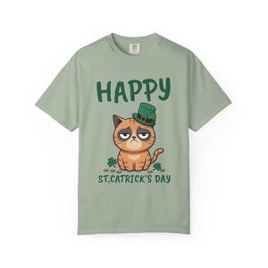 Op de afbeelding: Lichtgroen T-shirt met een cartoonkat met een groene St. Patrick's Day hoed. De tekst "HAPPY ST. CATRICK'S DAY" staat boven en onder de kattenillustratie. De kat heeft een humeurige uitdrukking.