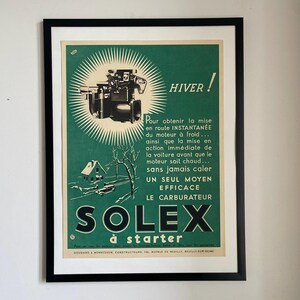 May include: Framed vintage Solex carburetor advertisement. The poster has a green background with a black and white illustration of a carburetor, a house, and a car. Text includes "HIVER!" and "SOLEX à starter."