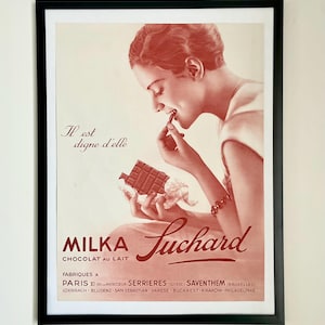 May include: Framed vintage advertisement for Milka Suchard chocolate. The poster features a woman enjoying a piece of chocolate. The text reads "Il est digne d'elle" and "Chocolat au Lait". The poster is in shades of red and white.