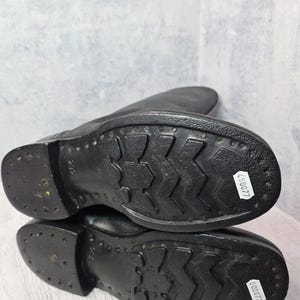 Puede incluir: Botas de cuero negro con suela texturizada. Las suelas tienen un patr&oacute;n distintivo para el agarre y est&aacute;n marcadas con una pegatina blanca. Las botas son probablemente para uso en exteriores y son duraderas.