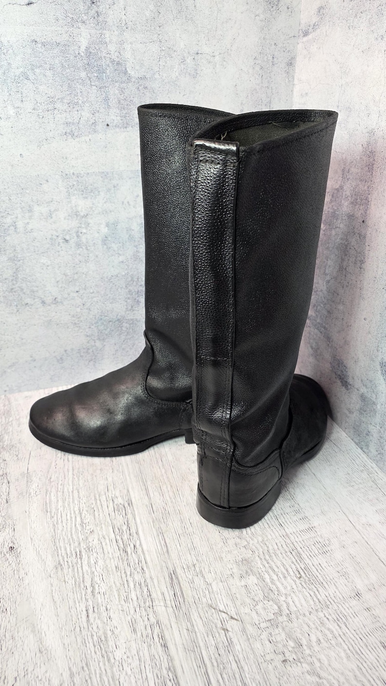 Puede incluir: Un par de botas negras de cuero hasta la rodilla. Las botas tienen un acabado liso y mate y un dise&ntilde;o cl&aacute;sico. Las suelas son planas y las botas parecen sin usar. Las botas miden aproximadamente 40 cm de altura.