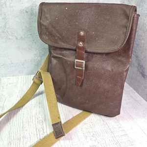 Könnte beinhalten: Braune Messenger-Tasche mit Klappenverschluss und beigem Schultergurt. Die Tasche hat eine rechteckige Form und einen Schnallenverschluss. Der Gurt ist verstellbar. Die Tasche ist aus strapazierfähigem Material.