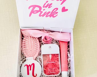 Peut inclure: Une boîte cadeau blanche avec le texte Pretty in Pink contenant une brosse à cheveux rose clair avec miroir, un ruban rose clair, un spray désinfectant pour les mains Touchland de 30 ml et un baume à lèvres Summer Fridays sur du papier déchiqueté.