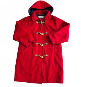 May include: A bright red wool-blend duffle coat featuring a hood, long sleeves, and four wooden toggle closures with braided rope loops. The interior of the hood is lined with a dark green and navy blue plaid fabric. An L.L. Bean label is visible.