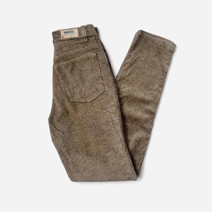 May include: Taupe corduroy trousers featuring a high-waisted design with a back pocket and a rectangular label on the waistband that reads MAKO. The fabric has a vertical ribbed texture, and the trousers include belt loops and a standard button closure.