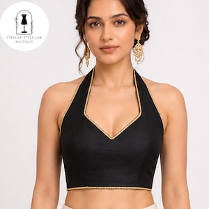 May include: A black sleeveless halter top featuring a deep V-neckline and gold trim along the edges. The garment includes a logo in the upper left corner with the text STELLAR STYLE LAB BOUTIQUE. The design is solid black with gold detailing.