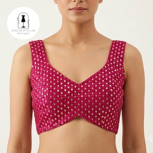 May include: A sleeveless fuchsia blouse featuring a deep V-neckline and a structured grid pattern embellished with small gold-toned metallic squares throughout the fabric. The garment has a cropped length and a fitted silhouette.