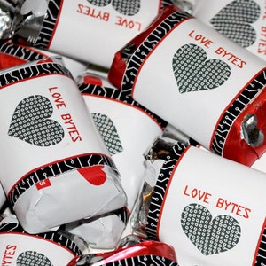 May include: A close-up of several small, red and silver wrapped chocolate candies with white labels that say "Love Bytes" and feature a black and white heart design.