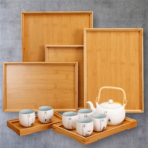 Könnte beinhalten: Eine Auswahl an Serviertabletts aus Bambus in verschiedenen Größen, zusammen mit einer weißen Keramik-Teekanne und passenden Teetassen. Die Teetassen und die Teekanne stehen auf kleineren Bambustabletts. Das Teeservice hat ein minimalistisches Design.