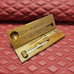 Op de afbeelding: Een houten wijnthermometerset in een rechthoekige scharnierende doos met een natuurlijke houtnerf. Het interieur bevat uitgesneden ronde uitsparingen voor twee glazen thermometers, waarvan één met een houten voet, en gedrukte instructies in het Nederlands.
