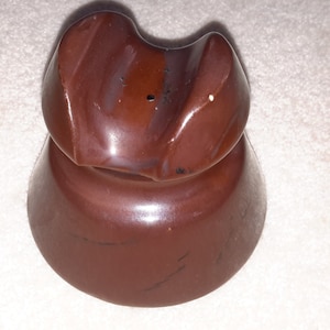 May include: A brown ceramic insulator with a rounded top and a wide base. The insulator has a small hole in the top.