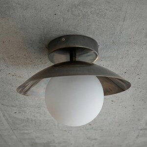 May include: A modern ceiling light fixture with a brushed metal finish and a white globe-shaped light. The fixture is mounted on a textured gray concrete ceiling, creating a minimalist aesthetic.