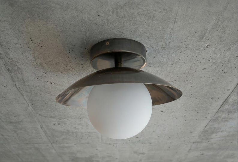 May include: A modern ceiling light fixture with a brushed metal finish and a white globe-shaped light. The fixture is mounted on a textured gray concrete ceiling, creating a minimalist aesthetic.