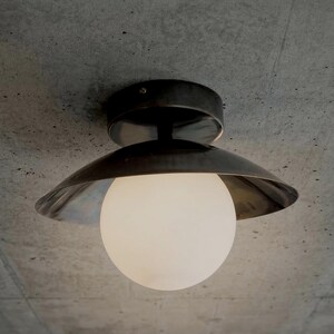 May include: A modern ceiling light fixture with a dark metal shade and a spherical, frosted glass bulb. The fixture is mounted on a concrete ceiling. The design is minimalist and industrial.