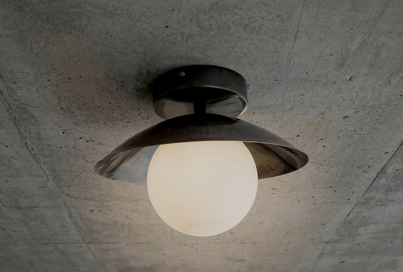 May include: A modern ceiling light fixture with a dark metal shade and a spherical, frosted glass bulb. The fixture is mounted on a concrete ceiling. The design is minimalist and industrial.