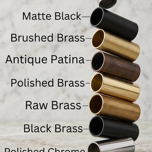 May include: A stack of cylindrical metal tubes in various finishes, including Brushed Chrome, Matte Black, and Polished Brass. The image also shows Antique Patina, Raw Brass, and Black Brass. Text labels identify each finish.