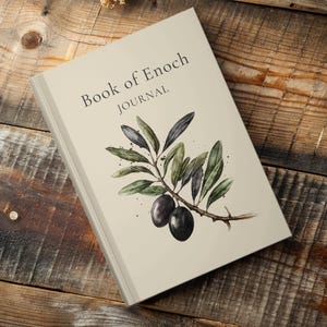 Peut inclure: Un journal intitulé "Book of Enoch" avec le mot "JOURNAL" en dessous. La couverture présente une illustration à l'aquarelle d'une branche d'olivier avec des feuilles vertes et deux olives foncées. Le journal est sur une surface en bois.
