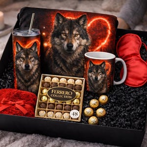 Op de afbeelding: Een zwarte geschenkdoos gevuld met een wolf-thema collectie. Inclusief een beker, kussen, mok, slaapmasker en een doos chocolade. De beker en mok tonen een wolfportret tegen een vurige achtergrond. Een rode strik siert een klein, pluizig item.