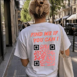 Peut inclure: Un t-shirt blanc à manches courtes avec le texte rouge "FIND ME IF YOU CAN!" imprimé au dos. Sous le texte se trouve un grand code QR carré de couleur rouge vif avec des marqueurs de coin noirs, centré sur le dos du vêtement.