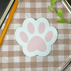 Puede incluir: Una pegatina blanca con forma de huella de pata con un diseño de huella de pata rosa. La pegatina está sobre un fondo a cuadros marrón y blanco.