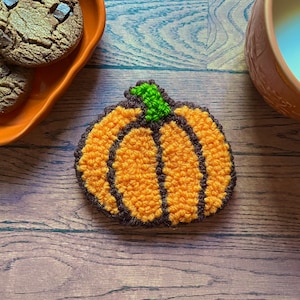 May include: A close-up of a small, orange and brown pumpkin-shaped craft, made with yarn. The pumpkin is on a wooden surface.