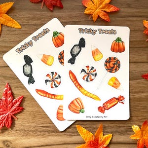 May include: Two white rectangular stickers with the text "Tricky Treats" and illustrations of Halloween candy, including pumpkins, candy corn, and lollipops. The stickers are surrounded by orange and red fall leaves.