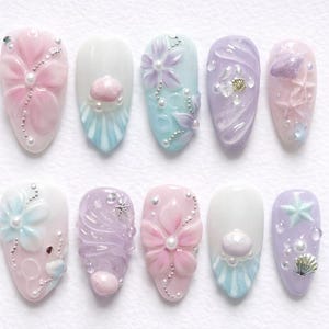 May include: A collection of ten almond-shaped false nails, each adorned with pastel hues and marine-inspired decorations. The designs feature flowers, shells, pearls, and starfish, offering a delicate and feminine appearance.