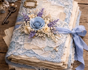 Op de afbeelding: Een vintage-stijl dagboek met een lichtblauwe kanten omslag, versierd met een blauwe roos, crèmekleurige bloemen en imitatieparels. Een lichtblauw lint wikkelt zich om het dagboek. Het dagboek heeft verouderde papieren pagina's en een klein gouden frame.