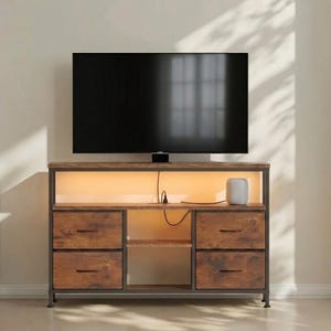 Puede incluir: Un mueble de TV de estilo rústico con un televisor negro encima. El mueble tiene cuatro cajones con un acabado de madera envejecida, un estante central abierto y una sección superior retroiluminada. Un pequeño altavoz blanco está en el estante superior.