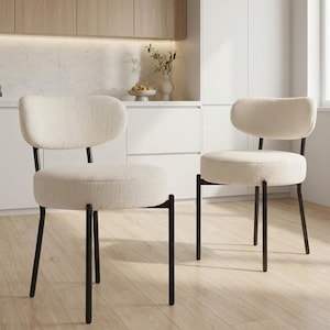 May include: Two cream-colored chairs with rounded backs and seats. The chairs have black metal legs and frames. The seats and backs are upholstered in a textured, fluffy fabric. The chairs are in a kitchen setting.