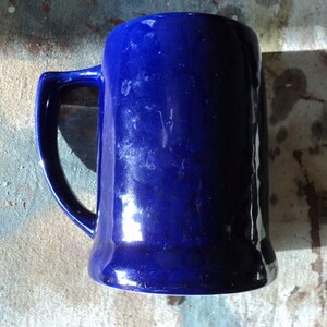 May include: A cobalt blue ceramic beer stein with a handle. The stein has a smooth, glossy finish.