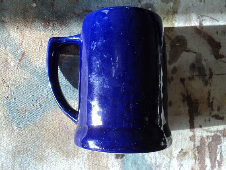 May include: A cobalt blue ceramic beer stein with a handle. The stein has a smooth, glossy finish.