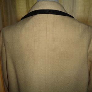 Pode incluir: Um blazer cor de creme com uma guarni&ccedil;&atilde;o preta em volta do colarinho. O blazer tem um tecido texturizado e uma &uacute;nica costura nas costas.