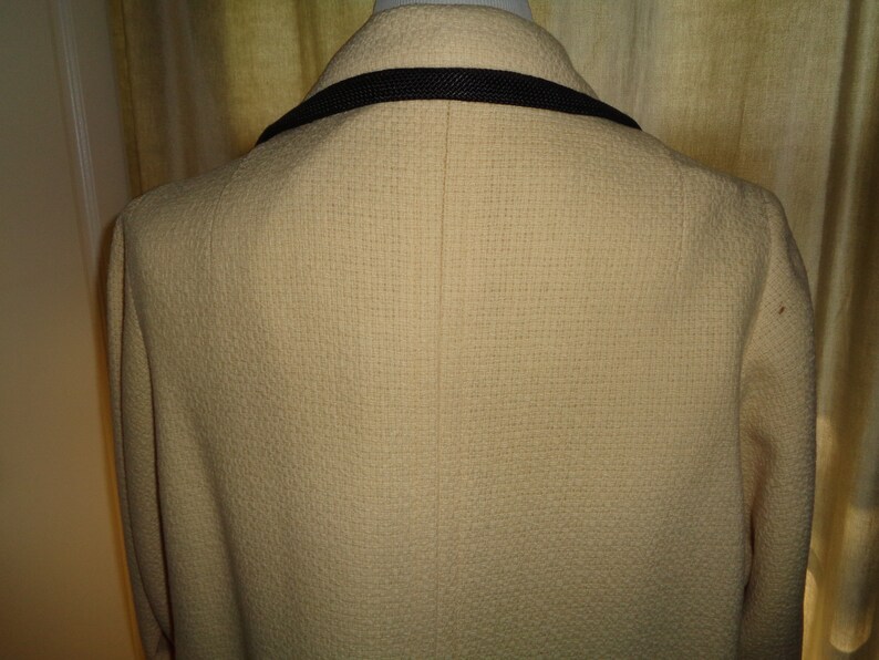 Pode incluir: Um blazer cor de creme com uma guarni&ccedil;&atilde;o preta em volta do colarinho. O blazer tem um tecido texturizado e uma &uacute;nica costura nas costas.