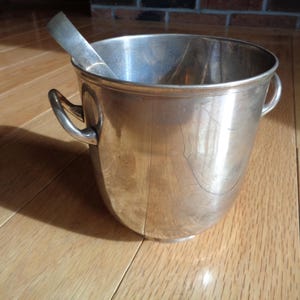May include: Silver ice bucket with two handles and a matching ice scoop. The bucket is made of polished metal and has a reflective surface.