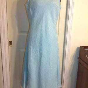 May include: A light blue sleeveless dress with a scoop neckline. The dress has a fitted bodice and a flared skirt that falls to the mid-calf. The hemline has a frayed edge. The dress is displayed on a black mannequin.