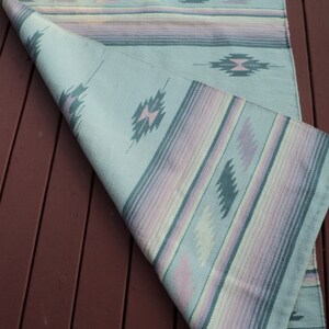 May include: A light blue and pink striped rug with a geometric pattern. The rug is folded in half and has a fringe on the end.