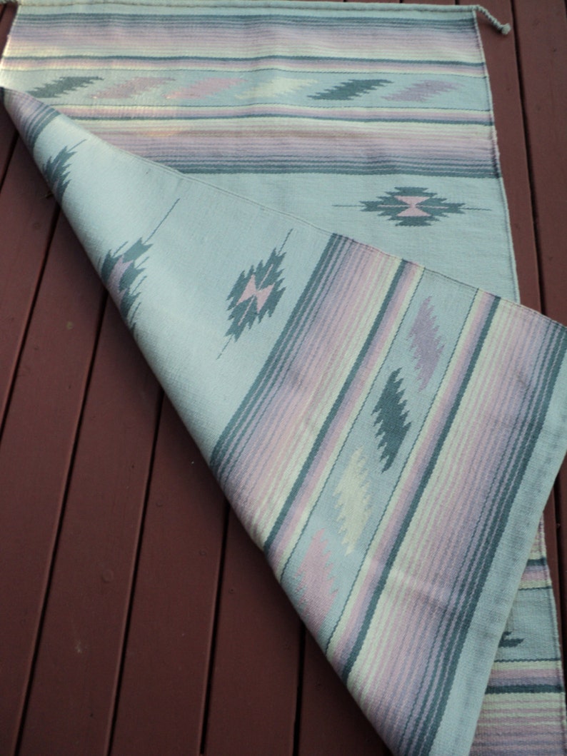 May include: A light blue and pink striped rug with a geometric pattern. The rug is folded in half and has a fringe on the end.