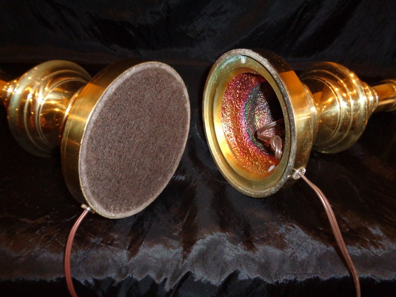 May include: Two vintage brass candlestick lamps with a warm, golden finish. The lamps have a classic, ornate design with a round base covered in brown felt. The interior of the lamp base has a colorful, iridescent finish, and a brown electrical cord.